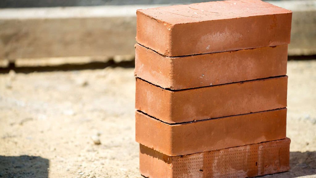 A stack of five red bricks is neatly arranged on a sandy construction site ground, a typical sight at locations featuring masonry supplies in Queens County.