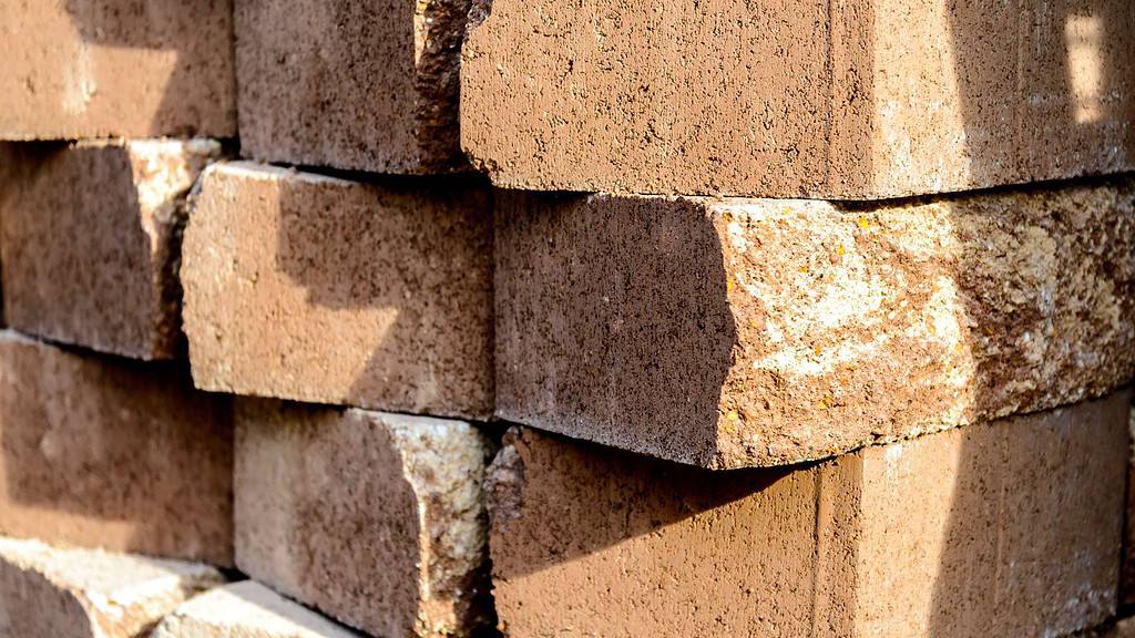 A close-up view of stacked brown bricks, with some sunlight casting shadows on the surface. The bricks display slightly rough and uneven textures, typical of construction materials found in Masonry Supplies Queens County.