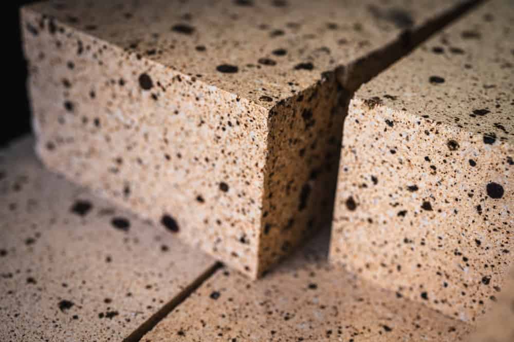 Close-up of two speckled beige stones with a rough texture. One stone is cut and staggered slightly above the other, revealing their irregular dark spots and granular appearance.